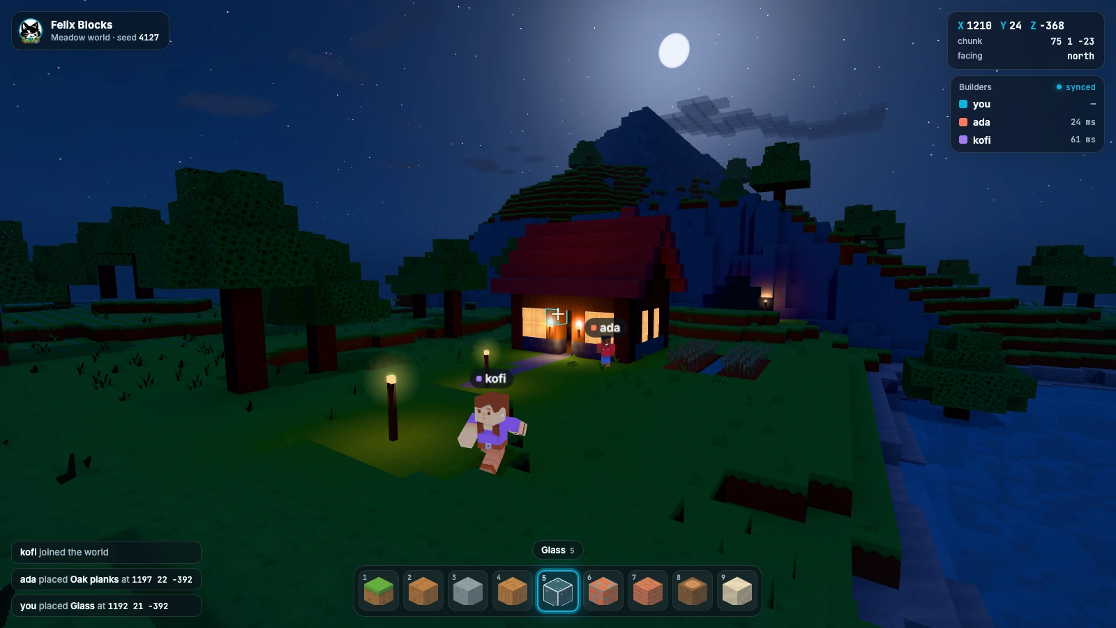 The same view at night under a moon, with lit windows, torches by the door and lanterns along the path